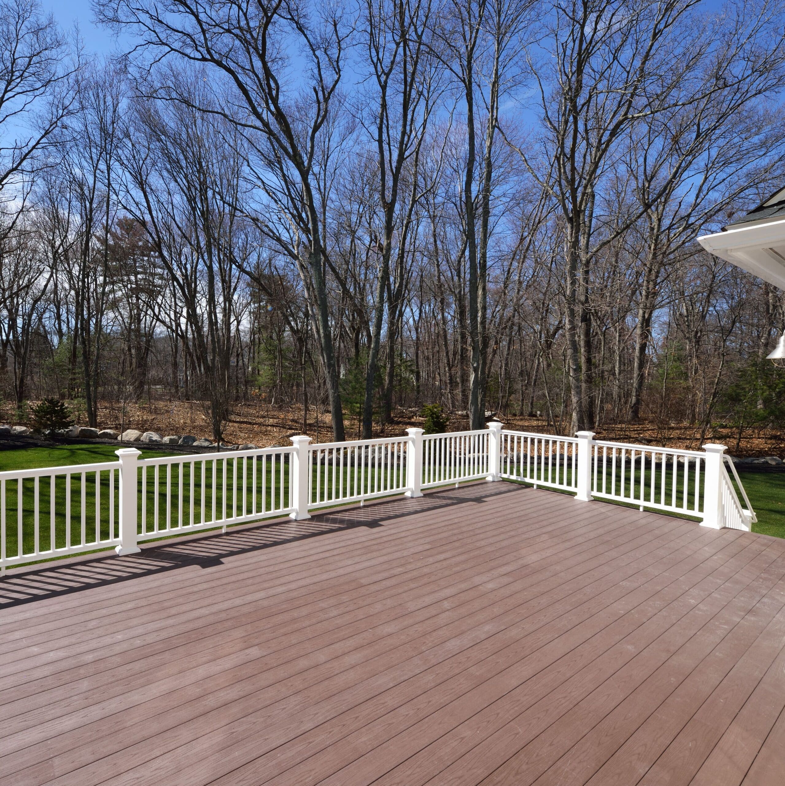 New backyard deck. White vinyl railings and composite brown boards. Large patio and garden space with a view to the woods.
