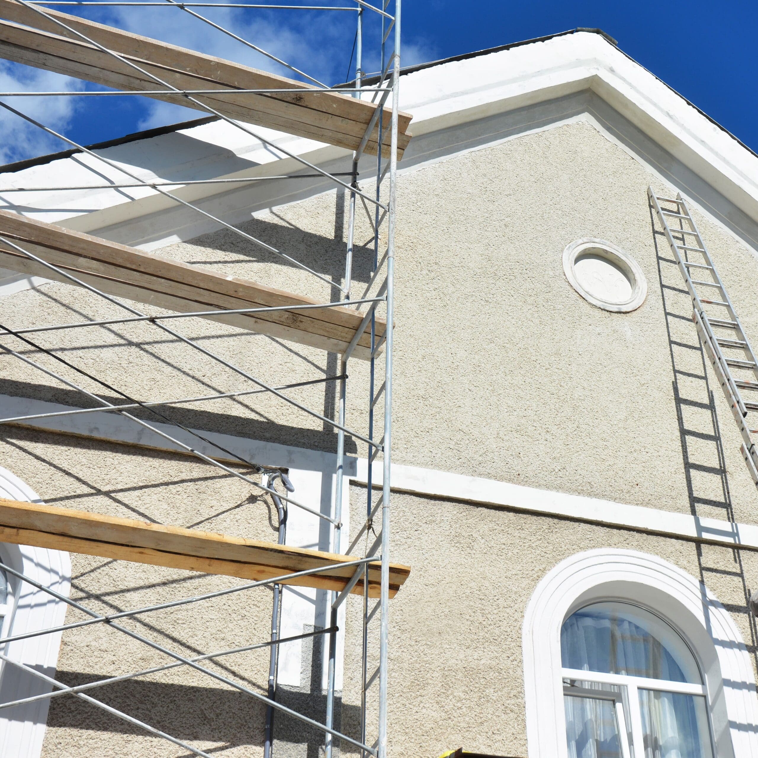 Painting and plastering exterior house scaffolding wall. Home facade insulation, sctucco and painting works during exterior wall renovations and repair. Contractors plastering house facade outdoor